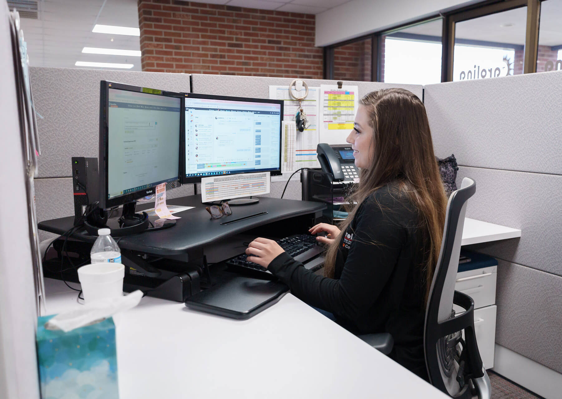 A Carolina Heating Service employee smiling while sitting at a desk and working on their computer - Carolina Heating Service Inc. A Carolina Heating Service employee smiling while sitting at a desk and working on their computer