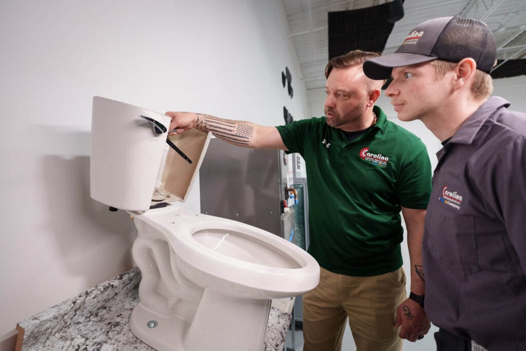 Two Carolina Heating Service technicians inspecting a display toilet - Carolina Heating Service Inc. Two Carolina Heating Service technicians inspecting a display toilet